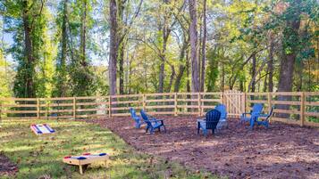 A fenced outdoor area with a shuffleboard table, several blue chairs, and a wooden bench.