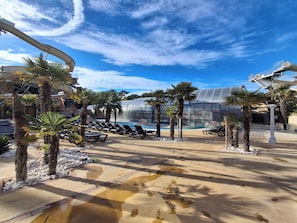 A resort pool area with lounge chairs, palm trees, and a large water slide.