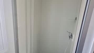 Pequeno espaço de chuveiro fechado, com porta de vidro, chuveiro e mangueira.