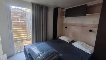 Een kamer met een bed, een raam met zonwering, een wandtelevisie en een stopcontact.
