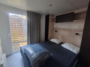 Ein Zimmer mit einem Bett, einem Fenster mit Jalousien, einem an der Wand befestigten Fernseher und einer Steckdose.
