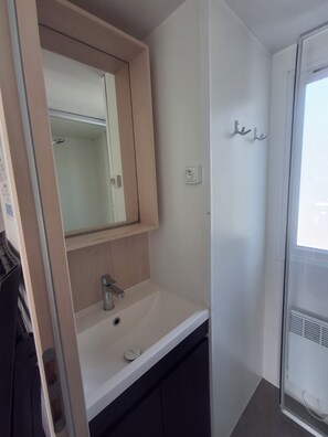 A bathroom with a white sink, a mirror, and a shower area. - Camping la pinède, les Mathes, bungalow premium, cottage, 37M2, tout confort. (Les Mathes)