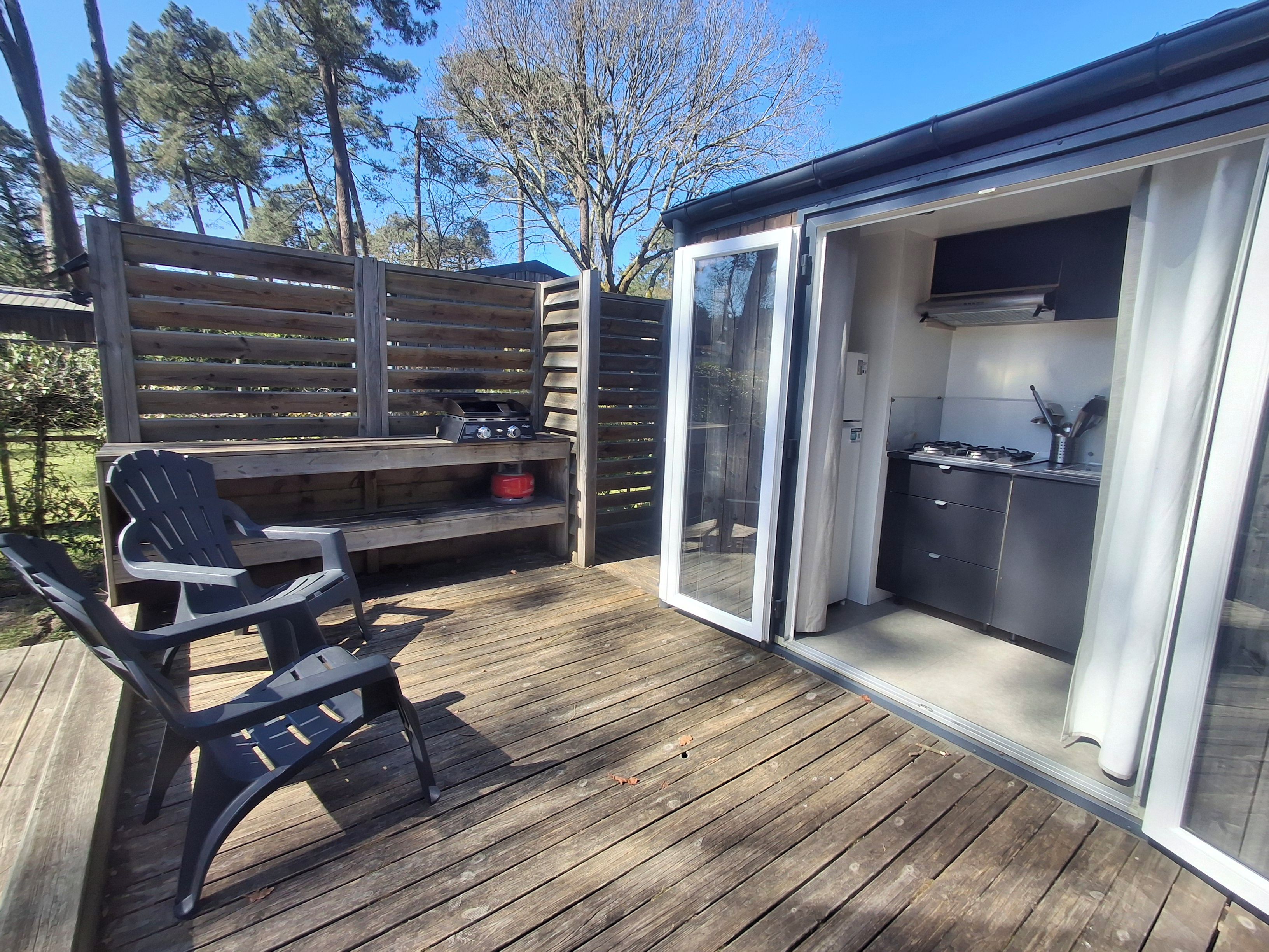 Eine Terrasse im Freien mit Grill, einem Esstisch und Stühlen sowie einer Glasgleittür, die zu einer Küche führt.