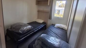 Una habitación pequeña con dos camas, un ventanal y estantería empotrada.