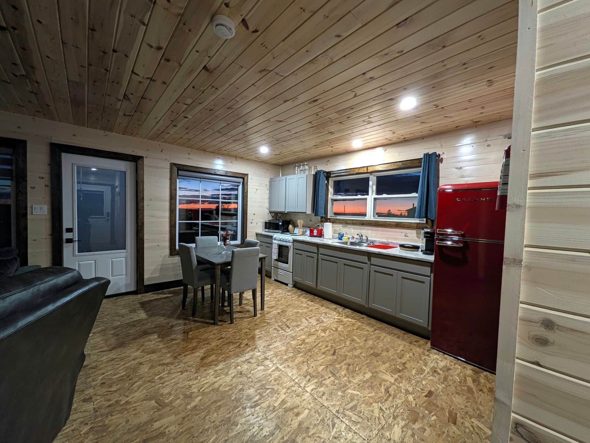 Een compacte keuken met een houten plafond, een eethoek met een tafel en stoelen, en een rode koelkast.