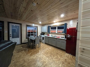 A compact kitchen with a wooden ceiling, a dining area with a table and chairs, and a red refrigerator.