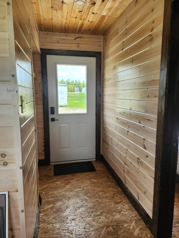 A narrow hallway with wooden walls and a door leading to an outdoor area.