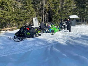 A snowy landscape with snowmobiles and a small building.
