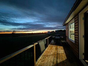 A wooden deck with a view of a sunset over a field.