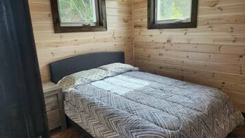 A single bed with a patterned bedspread in a room with wooden walls and two windows.