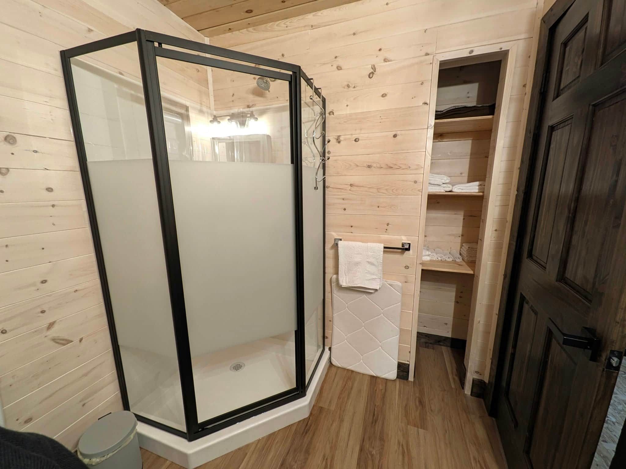 A shower enclosure with a glass door, wooden walls, and a tiled floor.
