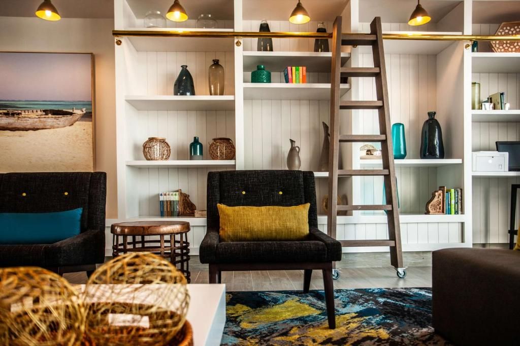 Een woonkamer met een zwarte fauteuil, een houten ladder en planken met decoratieve objecten.