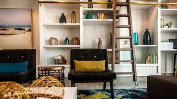Een woonkamer met een zwarte fauteuil, een houten ladder en planken met decoratieve objecten.