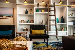 Een woonkamer met een zwarte fauteuil, een houten ladder en planken met decoratieve objecten.