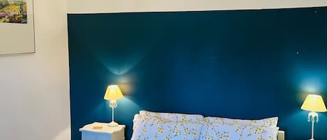 Un dormitorio con una cama, dos mesitas de noche con lámparas, un candelabro y un cuadro colgado en la pared.