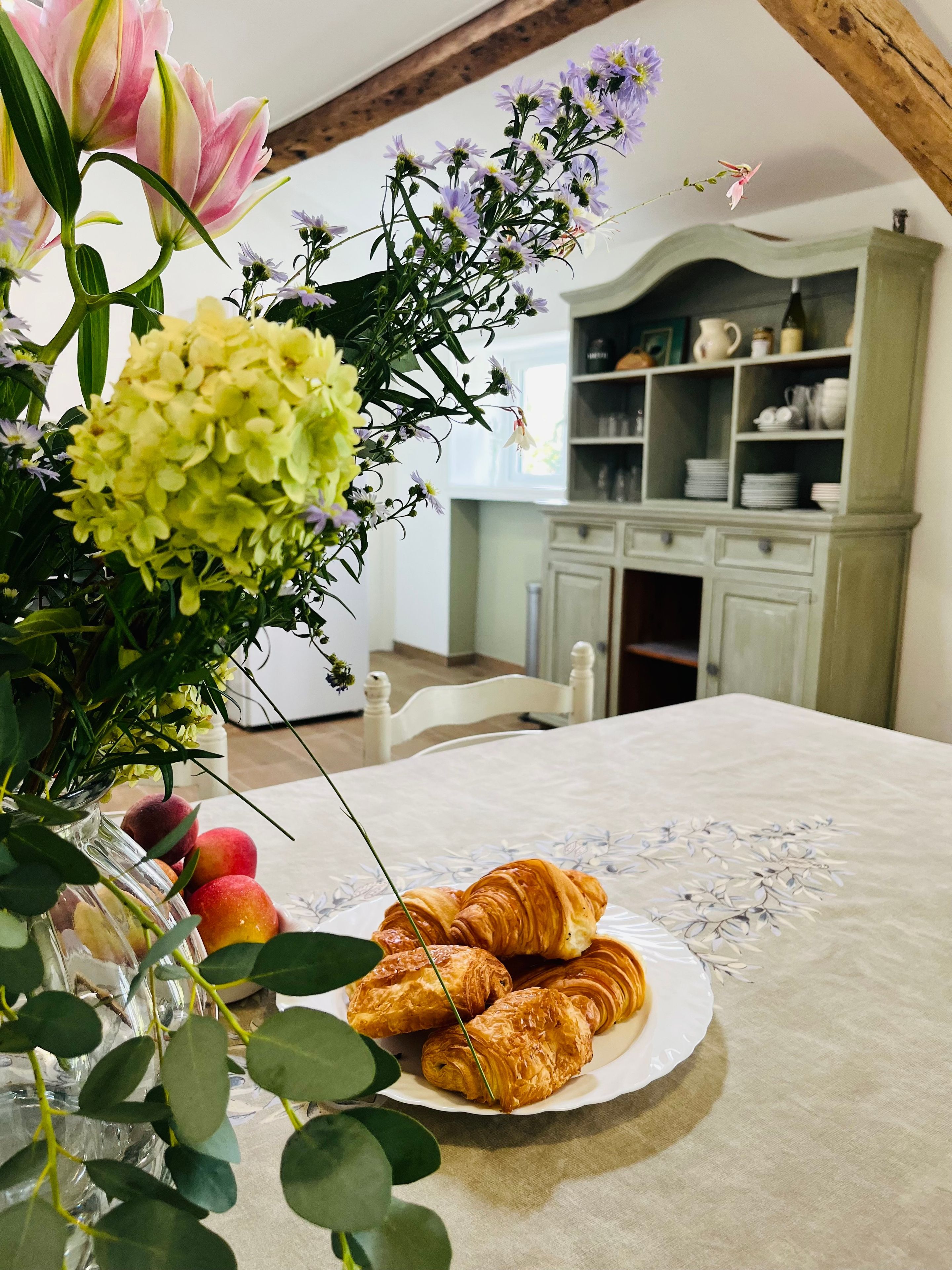 Een tafel met een tafelkleed met bloemen, een bord croissants en een bloevas.