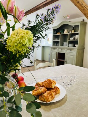 Une table recouverte d’une nappe à motifs floraux, une assiette de croissants et un vase rempli de fleurs.
