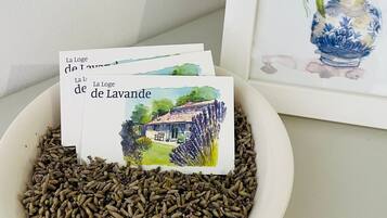 Un tazón de semillas de comino con un cuadro acuarela enmarcado de flores de lavanda y una postal de una casa con el texto 'La Loge de Lavande'.