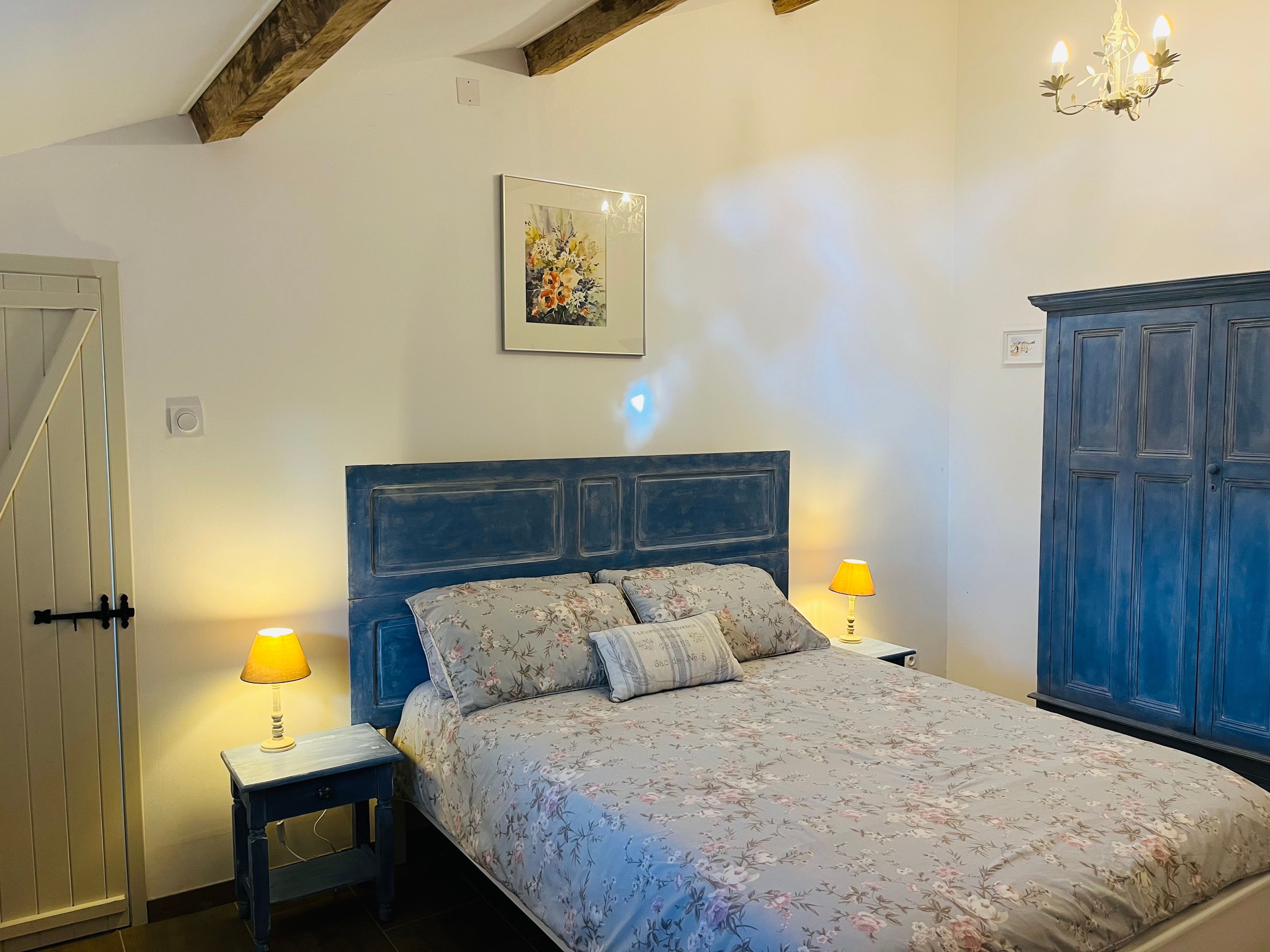 A bedroom with a bed, two bedside lamps, a wall-mounted picture, and a wardrobe.