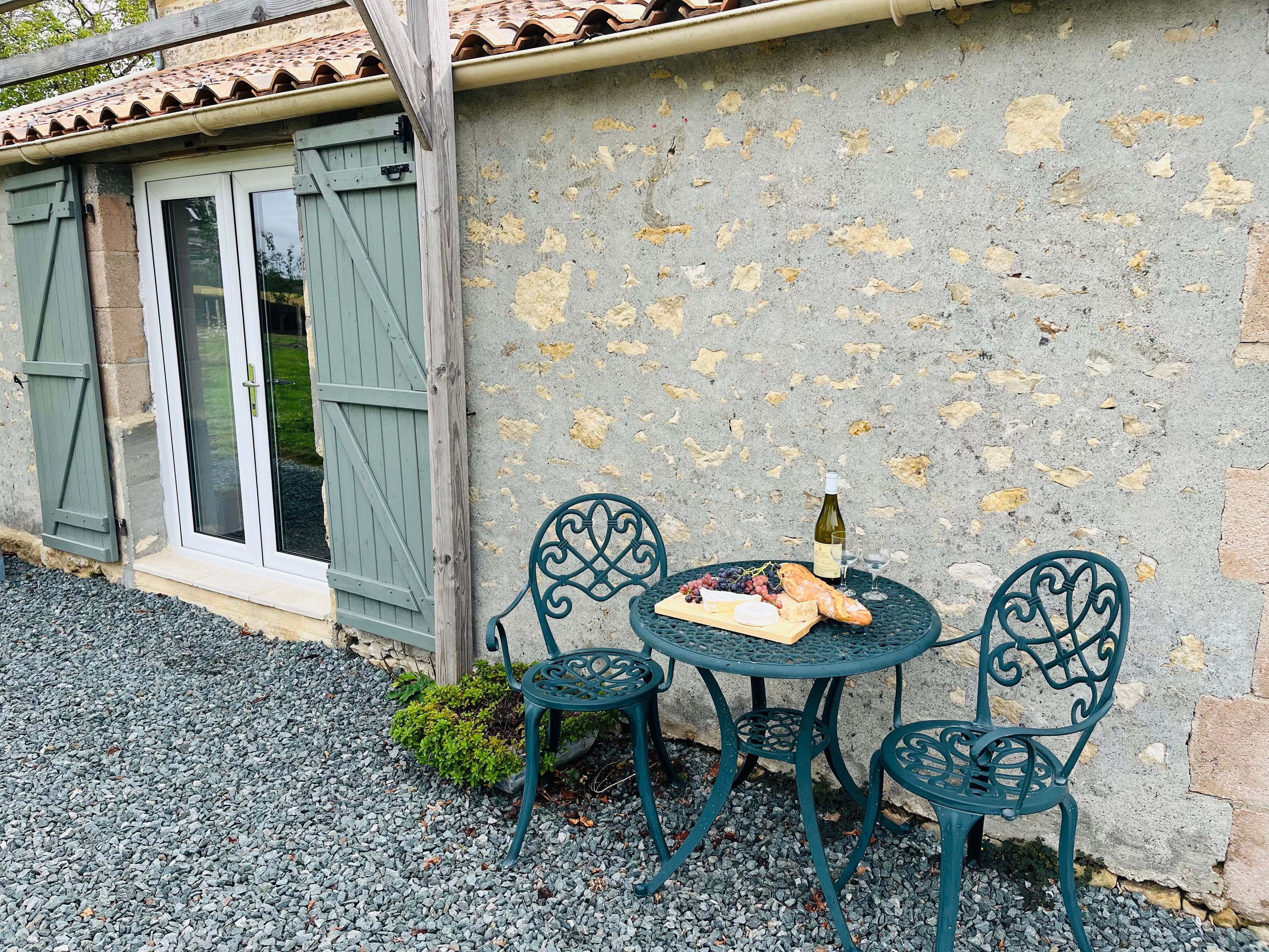 A rustic outdoor seating area with a table and chairs, a bottle of wine, and a small plant.