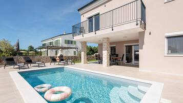 A modern two-story house with a swimming pool, outdoor seating, and a covered patio area.