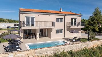 A two-story house with a swimming pool, outdoor seating, and a garden.