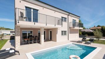 A two-story building with a swimming pool, outdoor seating, and a covered patio area.