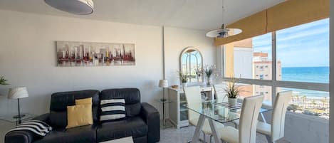 A modern living room with a black leather sofa, a glass dining table, and a cityscape painting on the wall.