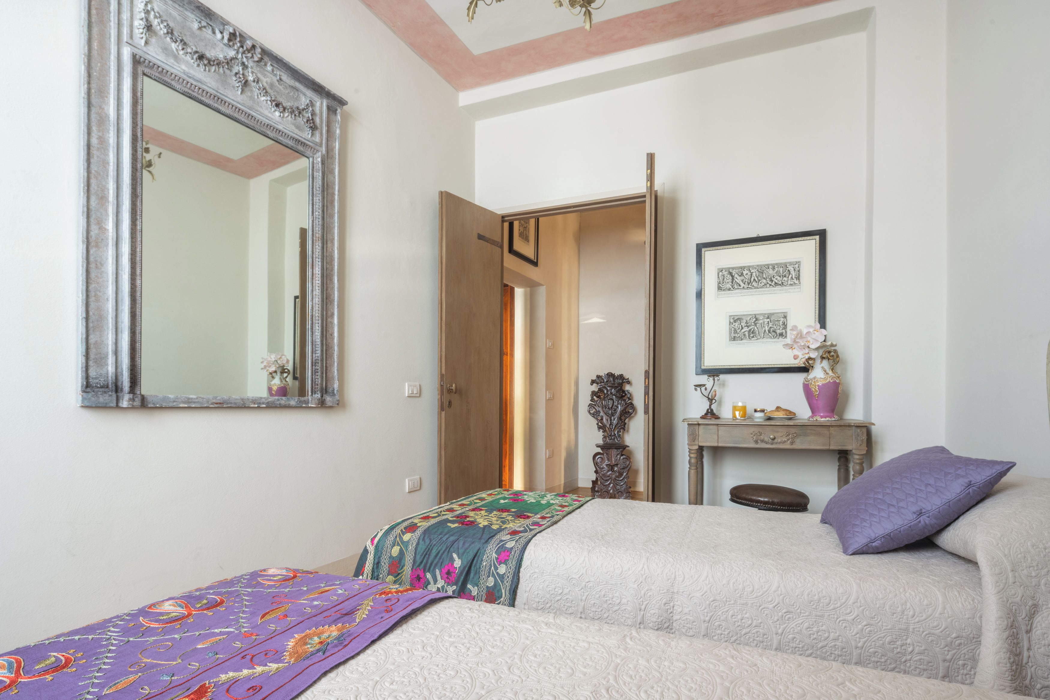 Una camera da letto con un letto, una cassettiera, uno specchio e una porta che dà su un'altra stanza.
