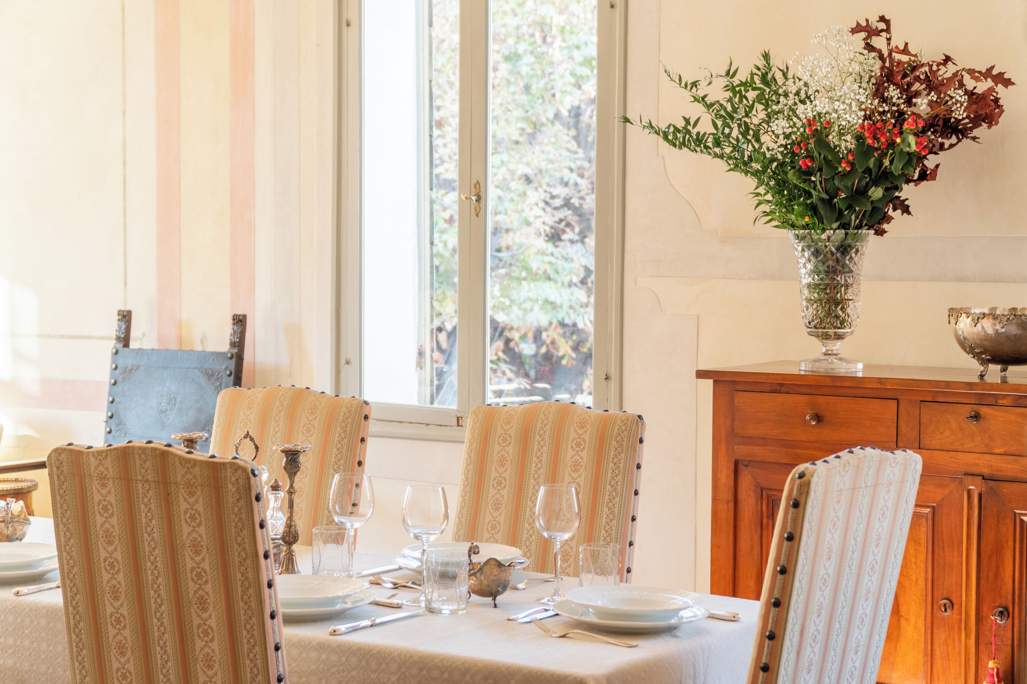 Comedor con una mesa dispuesta para cuatro, sillas con tapicería estampada, un florero con flores y un aparador de madera.