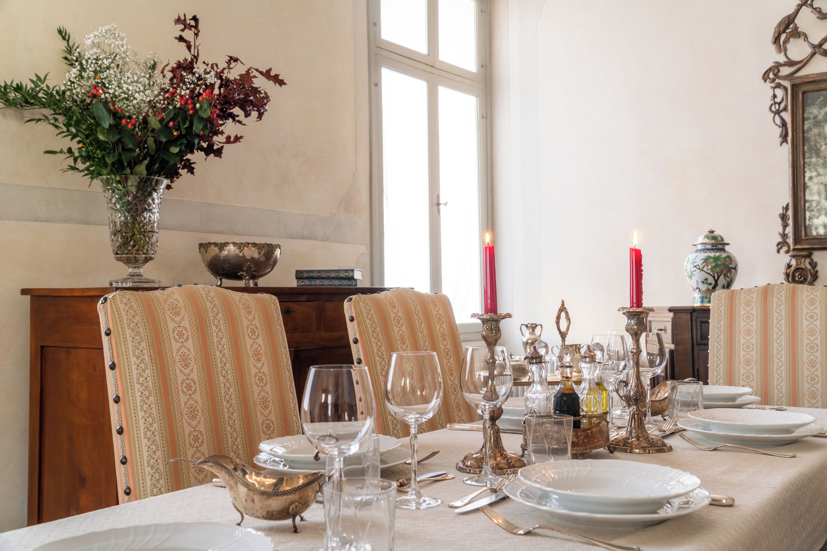 A dining table set with plates, glasses, and cutlery, a vase with flowers, and a candle.