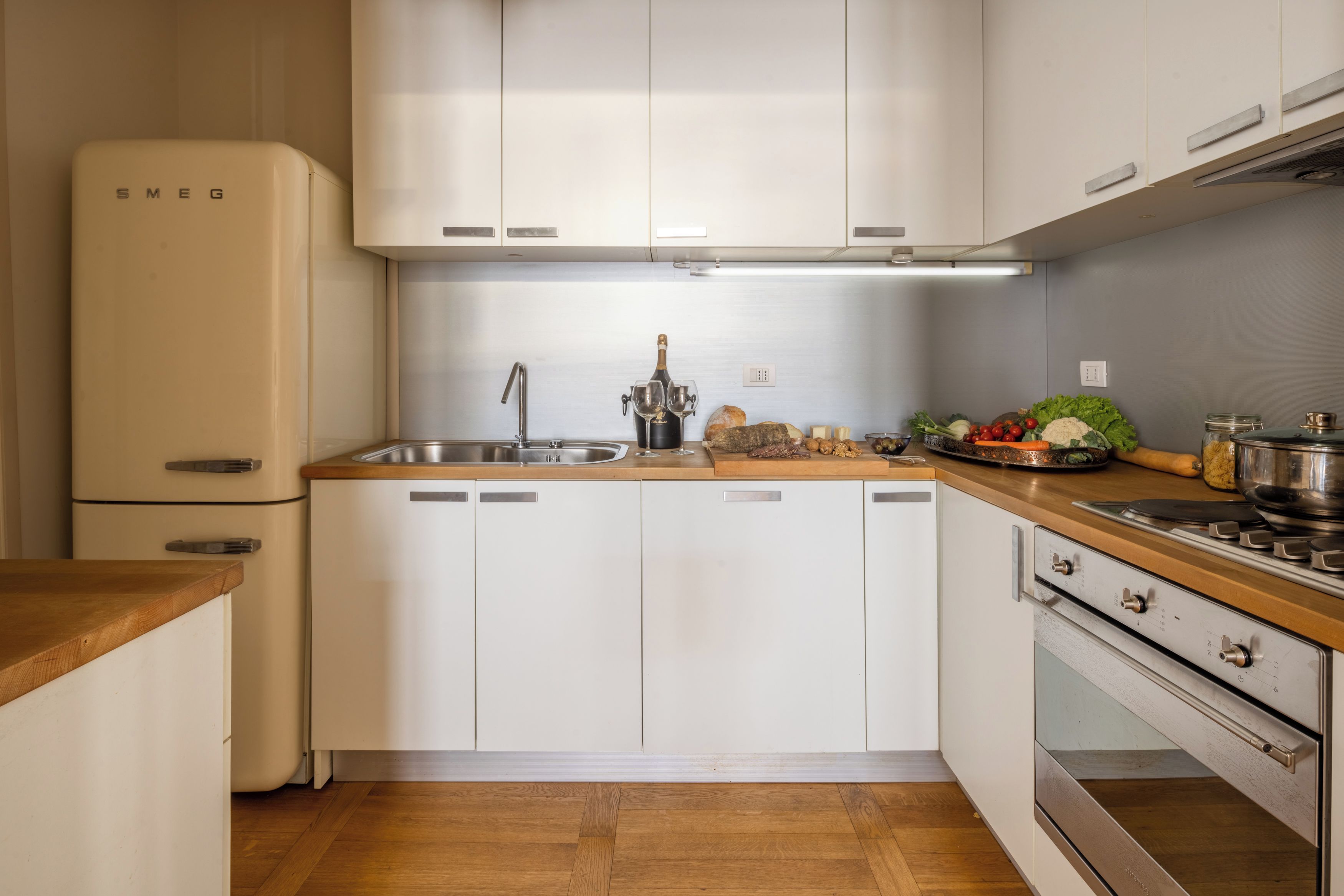 Une cuisine avec des meubles blancs, un évier en acier inoxydable, un four encastré et un plan de travail en bois.