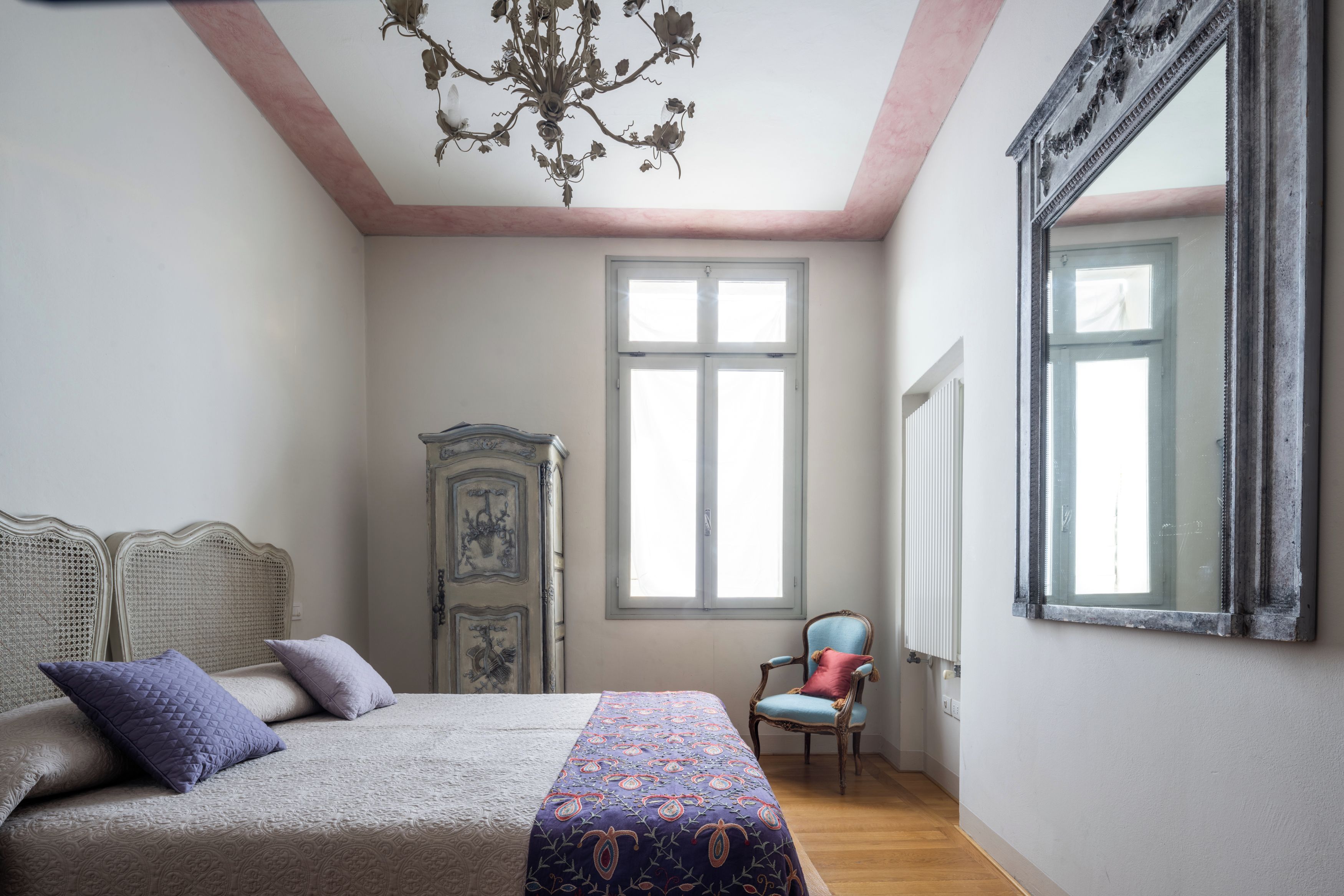 A bedroom with a bed, a chair, a wardrobe, and a large mirror.