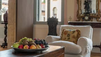 Ein Zimmer mit einem weißen Sessel, einem Holztisch mit Obstschale und Blick auf Gebäude durch ein Fenster.