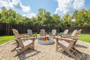 A circular fire pit with chairs around it, set on gravel, with a wooden fence and trees in the background. - 🌰 Acorn Lodge: Resort Views, Hot Tub, Fire Pit, & Mini Golf, Sleeps 12 (Sevierville)