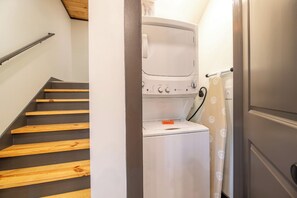 A laundry area with a washing machine, a dryer, and a staircase with wooden steps. - 🌰 Acorn Lodge: Resort Views, Hot Tub, Fire Pit, & Mini Golf, Sleeps 12 (Sevierville)