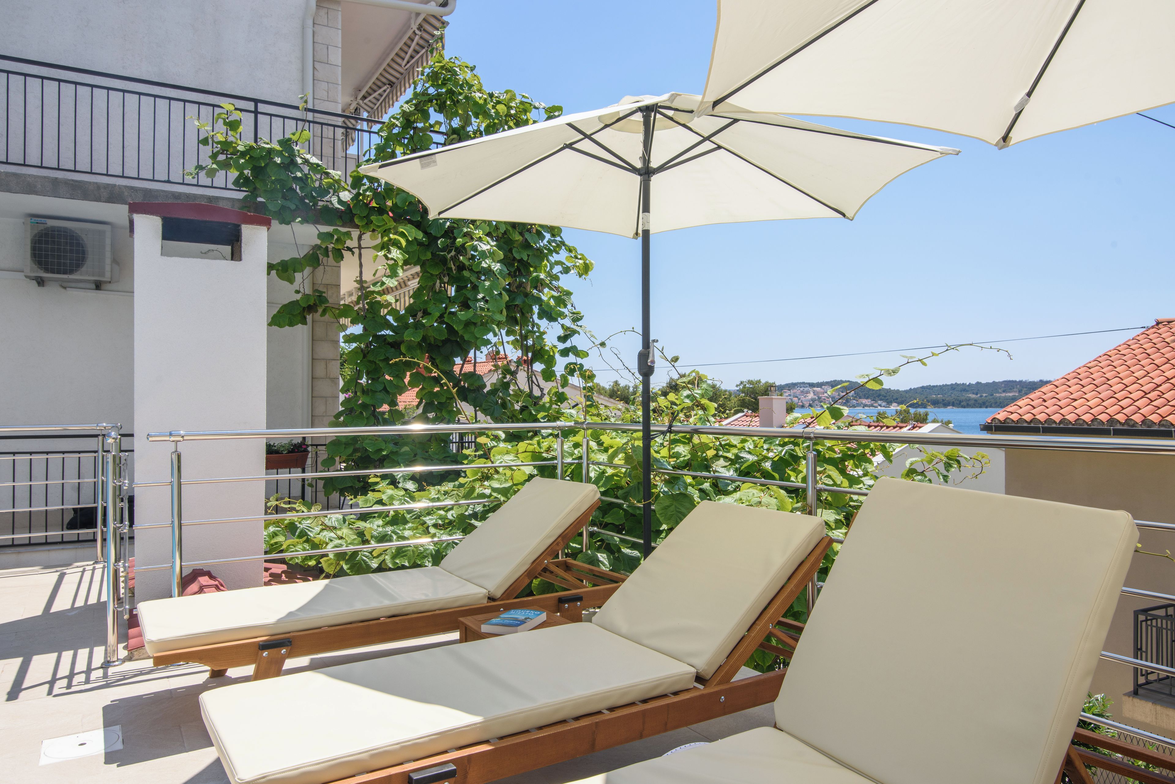 A balcony with two lounge chairs and a large umbrella, overlooking a scenic view with greenery and buildings.