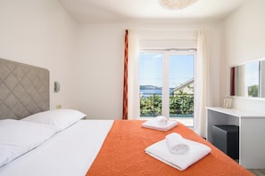 A hotel room with a bed, a desk, and a view of the outdoors. - A3 – 90 m2 apt with shared pool, big terrace and garden, just 50m from the beach (Mastrinka)