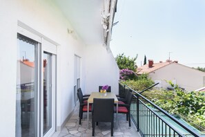 A balcony with a table and chairs, a view of the street, and a railing. - A3 – 90 m2 apt with shared pool, big terrace and garden, just 50m from the beach (Mastrinka)