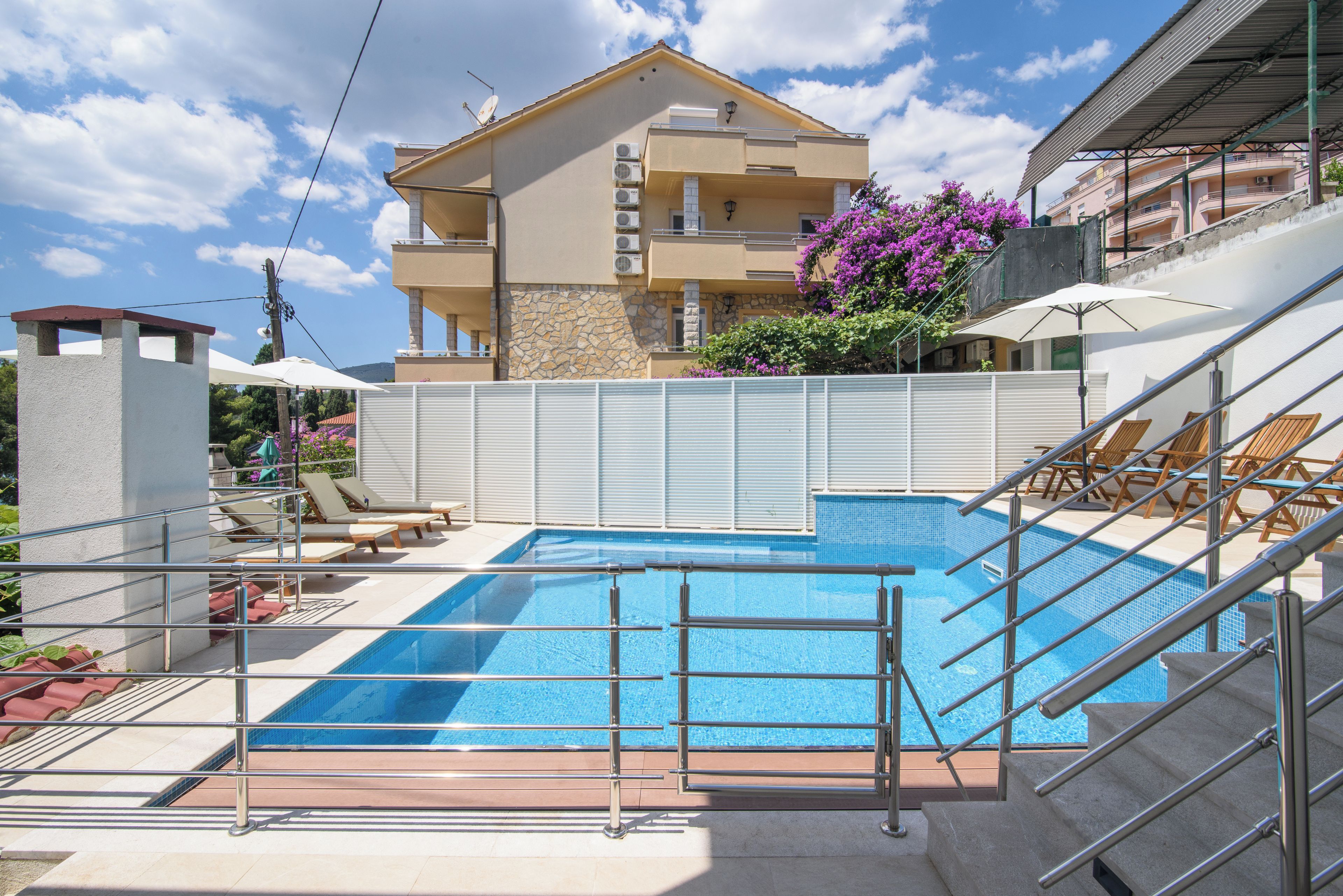 Une piscine avec une rambarde en métal, un escalier et un bâtiment doté de balcons en arrière-plan.
