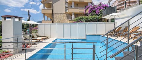 A swimming pool with a metal railing, a staircase, and a building with balconies in the background.