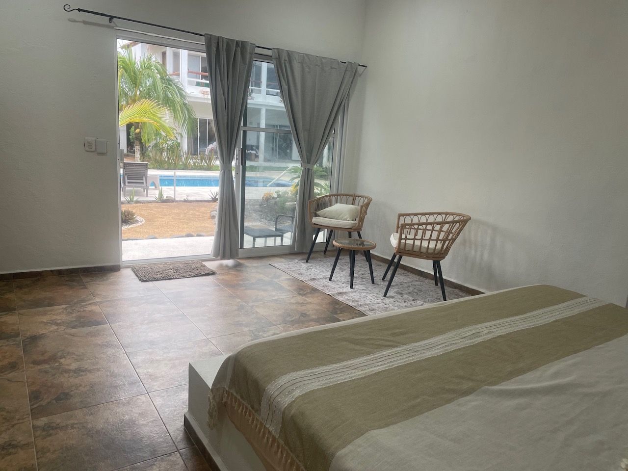 Une chambre avec un lit, une chaise et une vue sur une piscine, visible à travers une porte coulissante.