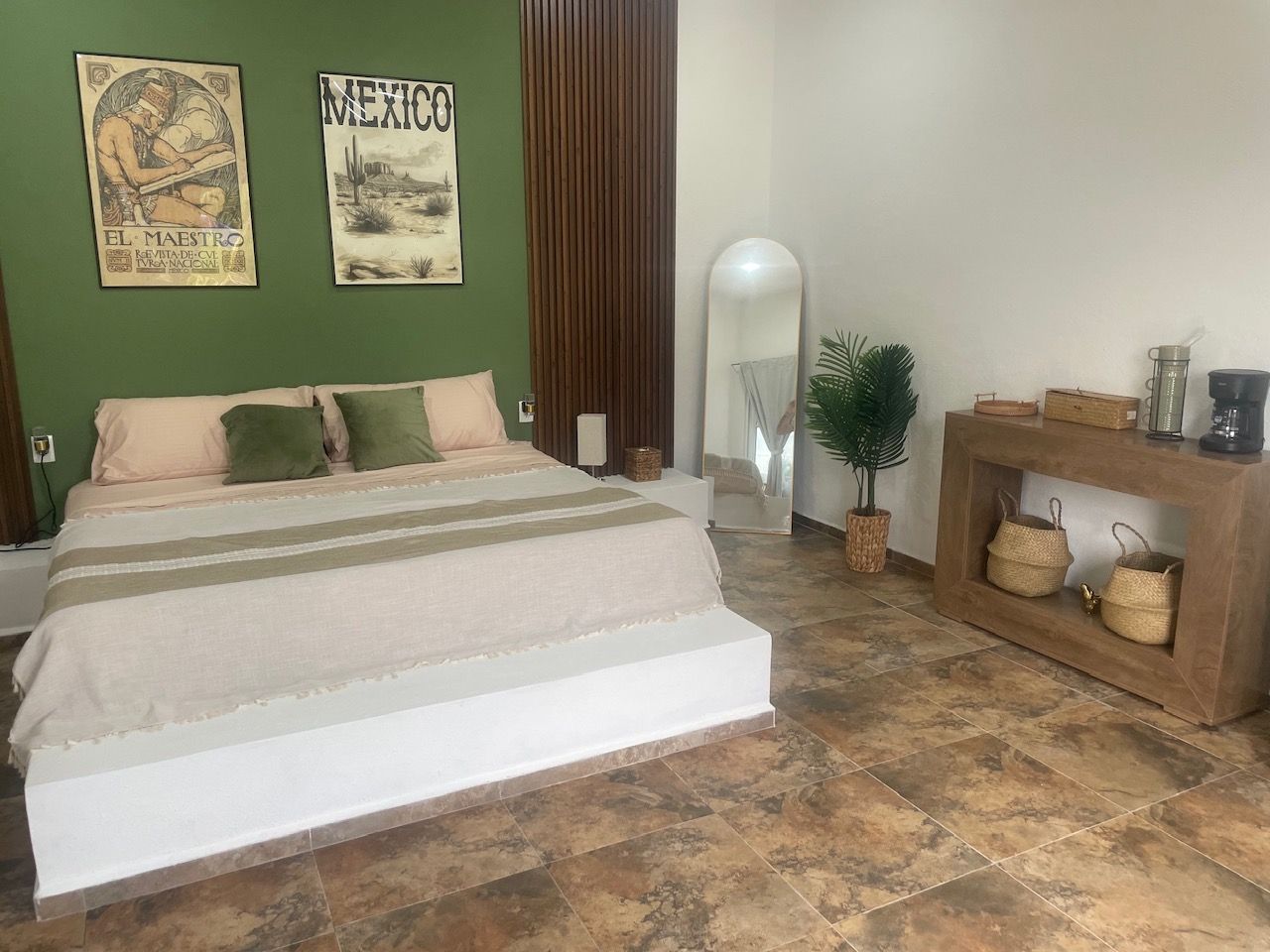 A bedroom with a large bed, green walls, and a wooden console table with baskets.