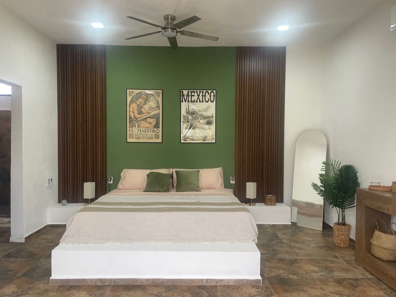 A bedroom with a large bed, two wall-mounted lamps, a ceiling fan, and two framed pictures.