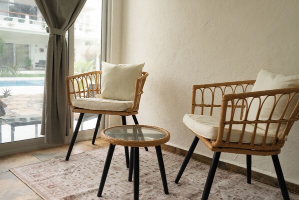 Two wicker chairs with cushions, a glass table, and a patterned rug in a room with a large window.