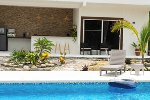 A pool area with lounge chairs, a small garden with rocks and plants, and a modern building with a stone wall and large windows. - King Suite - Casa Corazon Zen in Barra De Potosi with pool, 3 min. walk to beach (Barra de Potosí)