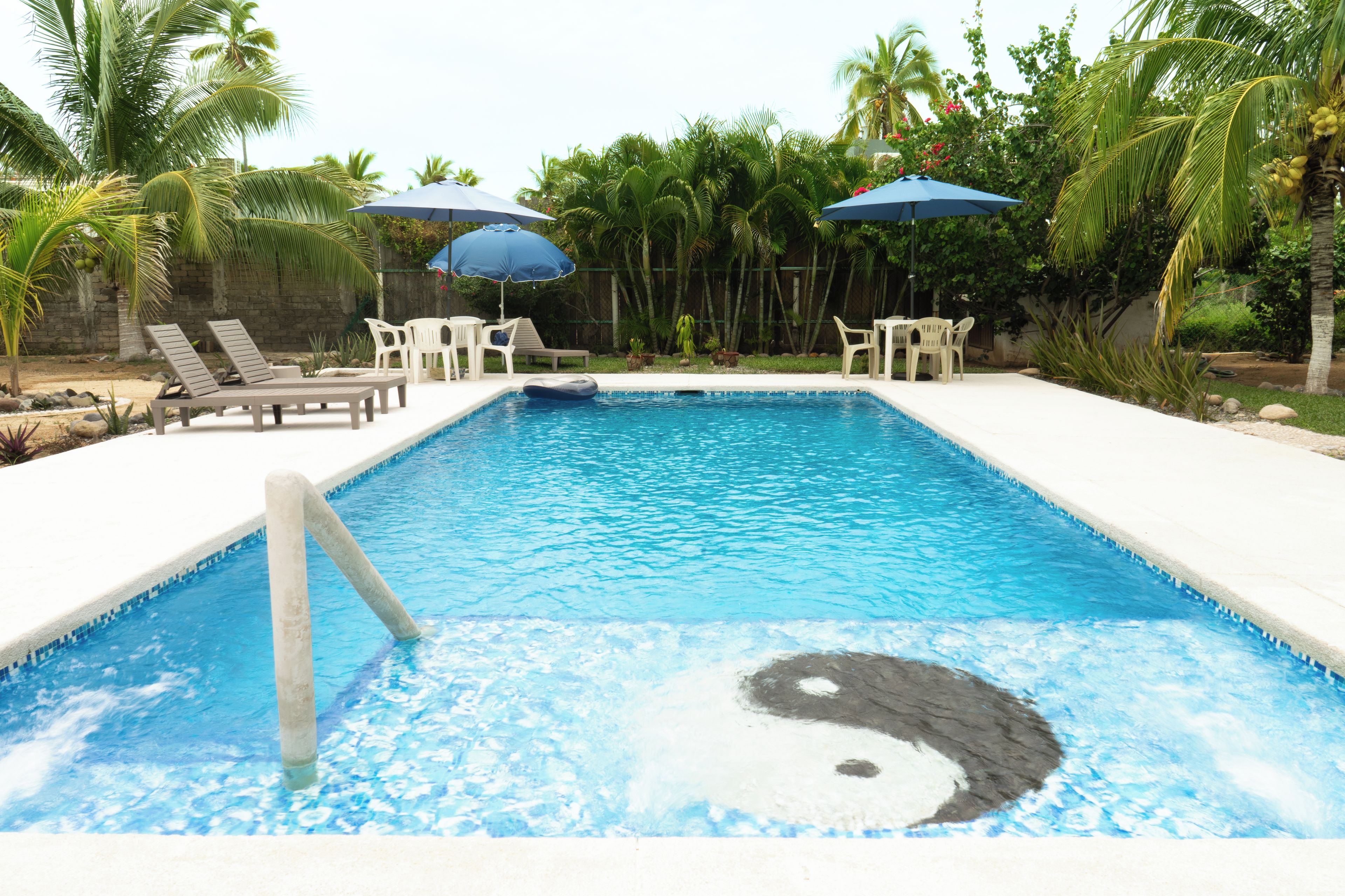 A rectangular swimming pool with a clear blue center, surrounded by lounge chairs and umbrellas.