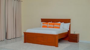 A bedroom with a wooden bed, white bedding, and orange pillows. - The Mana Hotel (Zanzibar)