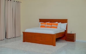 Une chambre à coucher avec un lit en bois, du linge de lit blanc et des oreillers orange.