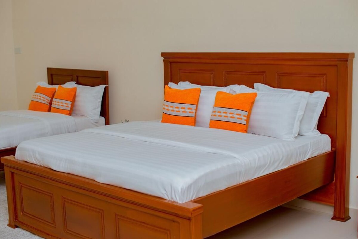 Two single beds with wooden headboards and white bedding, one with orange pillows and the other with white pillows.